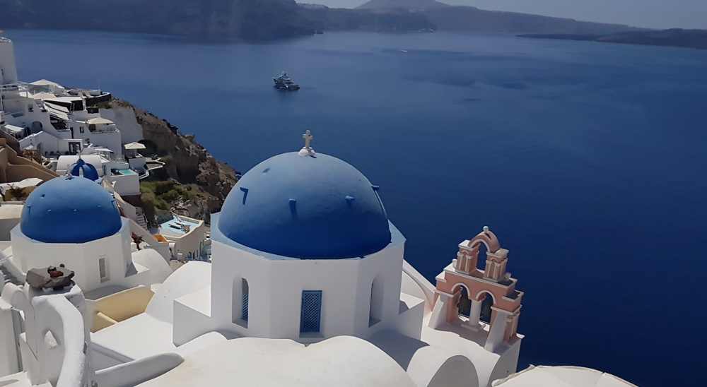 Naxos Greece: Travel Guide 2023 22 Phot of the blue domes and church bells of Santorini with the Aegean Sea below the lip of the caldera, Santorini, Greece