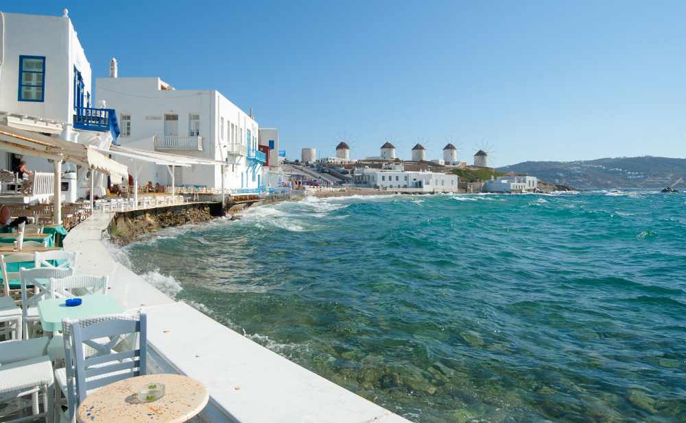 Naxos Greece: Travel Guide 2023 20 Photo of the shore at Mykonos with restaurants on the seafront, and windmills on the hills further around the shore